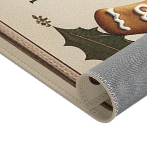 May include: A beige doormat with a gingerbread man design and the text "I'm dreaming of a white Christmas". The doormat has a brown border and a green holly leaf design. The doormat is rolled up, showing the grey backing.
