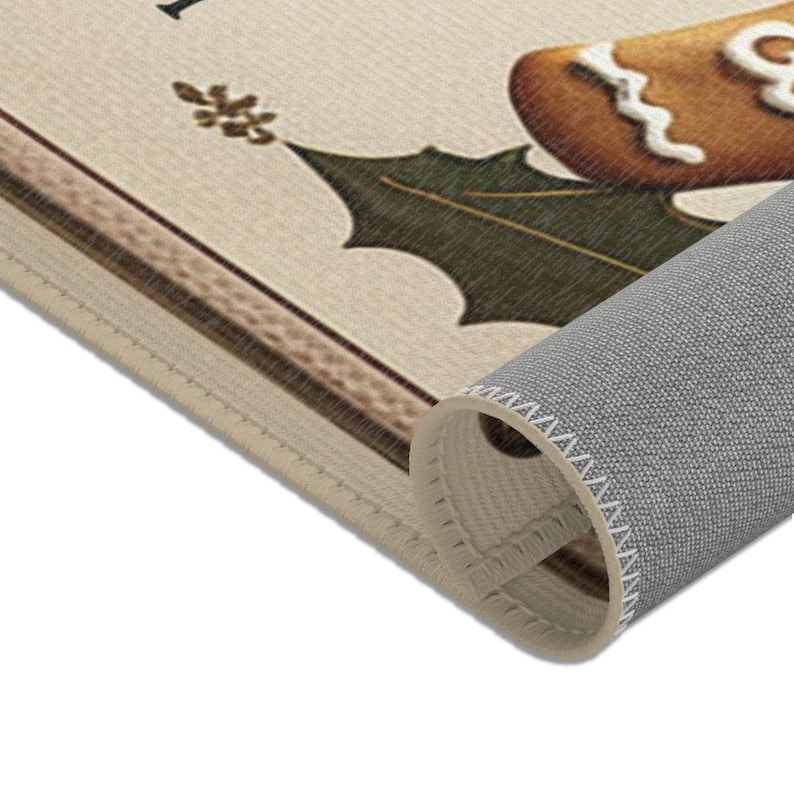 May include: A beige doormat with a gingerbread man design and the text "I'm dreaming of a white Christmas". The doormat has a brown border and a green holly leaf design. The doormat is rolled up, showing the grey backing.