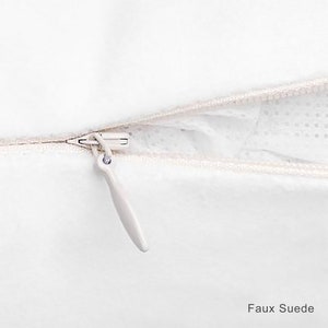 May include: Close-up of a white zipper on a pillow cover. The zipper is open and the fabric is faux suede.