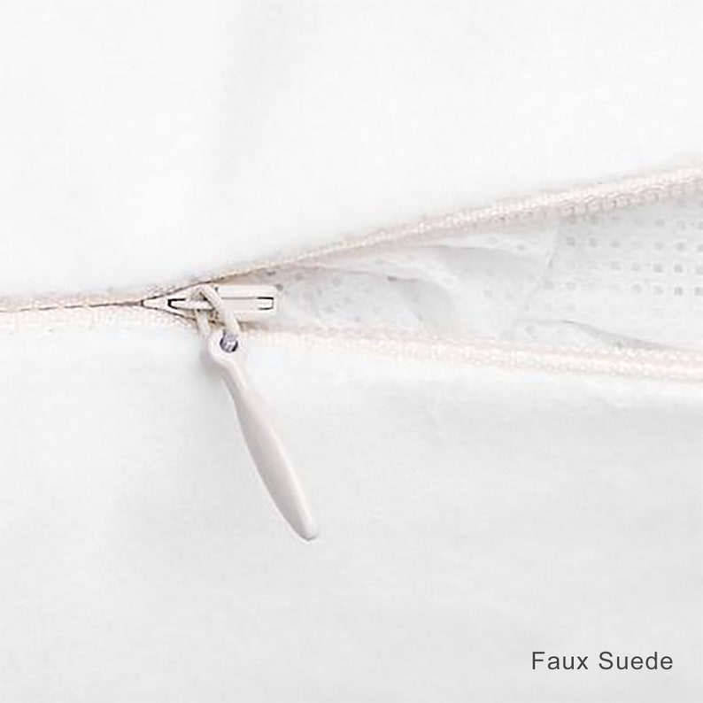 May include: Close-up of a white zipper on a pillow cover. The zipper is open and the fabric is faux suede.