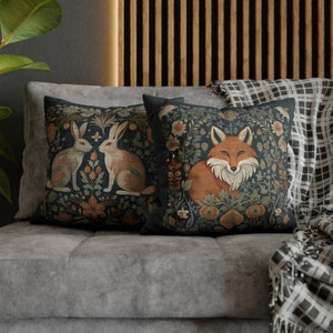 May include: Two decorative throw pillows with a dark blue background and intricate floral patterns. One pillow features a fox with orange fur and the other features two rabbits with white fur.