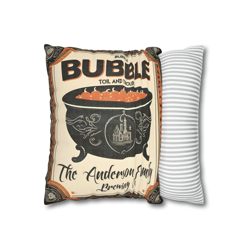 May include: A decorative pillow with a vintage-style illustration of a cauldron with orange liquid and the text "Bubble Toil and Trouble The Anderson Family Brewing It". The pillow is paired with a gray and white striped pillow.