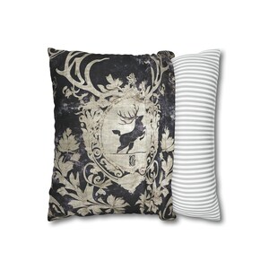 May include: A decorative throw pillow with a black background and a vintage-style design featuring a stag with antlers and ornate floral details. The pillow is paired with a white pillow with gray stripes.