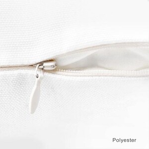 May include: Close-up of a white zipper on a white pillow cover. The zipper is made of metal and has a white pull tab. The pillow cover is made of polyester.