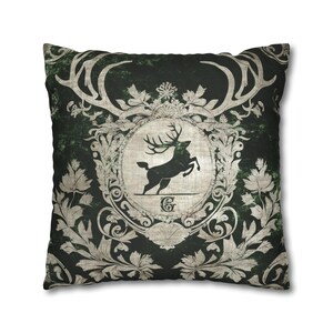 May include: A green and white decorative pillow with a stag silhouette in a crest. The stag is leaping and has large antlers. The crest is surrounded by ornate floral designs.