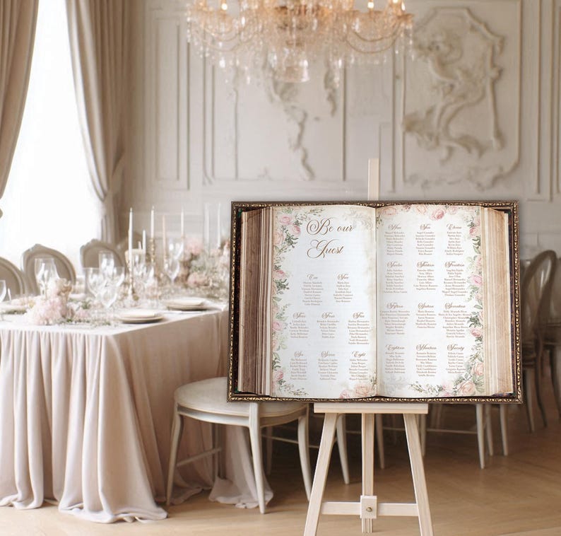 A beautiful open storybook seating chart featuring pale blush pink florals on the pages with Be Our Guest and your custom seating chart printed in an elegant vintage gold font. Great for a fairytale wedding or for a Once Upon a Time celebration.