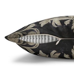 May include: A decorative throw pillow with a black background and a white floral pattern. The pillow has a zipper closure and a striped fabric lining.