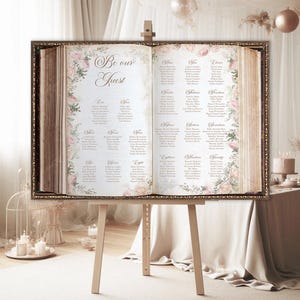 May include: A vintage-style wedding seating chart displayed on an easel. The chart is printed on a cream-colored background with a floral design and the words "Be our Guest". The chart lists guest names and table assignments.