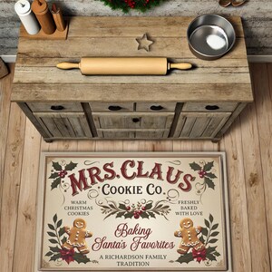 May include: A cream-coloured kitchen rug with a vintage-style design featuring the text "Mrs. Claus Cookie Co." and a gingerbread cookie illustration. The text reads "Baking Santa's Favourites, A Richardson Family Tradition."