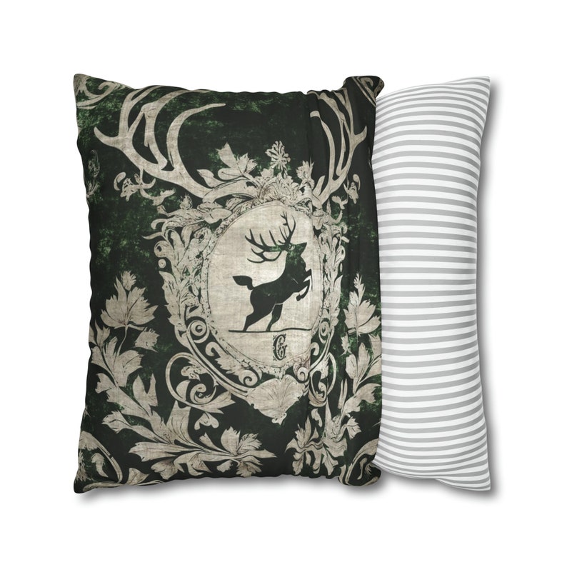 May include: A green pillow with a white deer and antlers in a decorative frame. The pillow has a distressed, vintage look. The pillow is paired with a white and gray striped pillow.