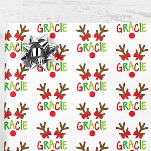 May include: White wrapping paper with a repeating pattern of brown reindeer antlers, red bows, and the name "GRACIE" in green, red, and white letters.