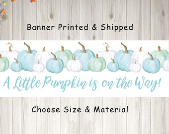 May include: A white banner with a blue and green watercolor pumpkin border. The text "A Little Pumpkin is on the Way!" is in blue. The text "Banner Printed & Shipped" and "Choose Size & Material" are in black.
