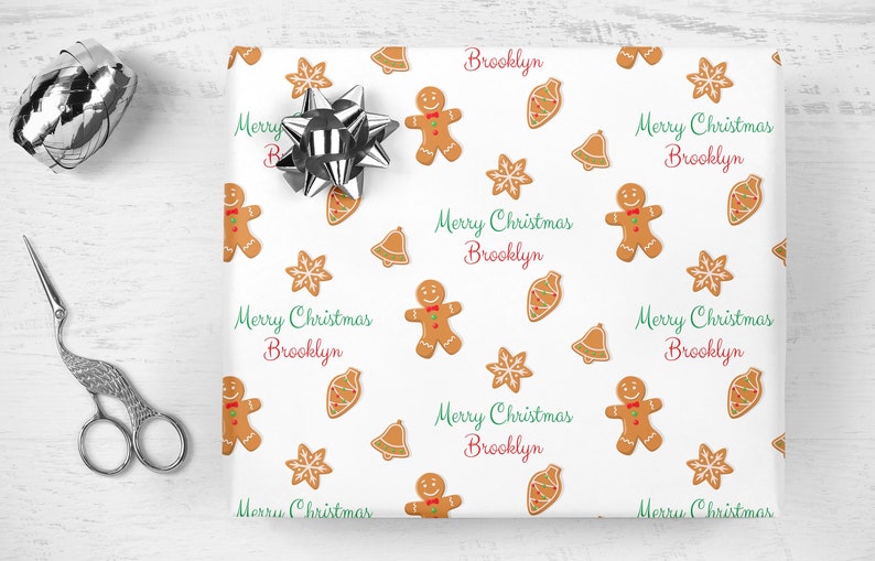 Op de afbeelding: Wit inpakpapier met een herhalend patroon van gingerbreadmen, sneeuwvlokken, bellen en de tekst "Merry Christmas Brooklyn".