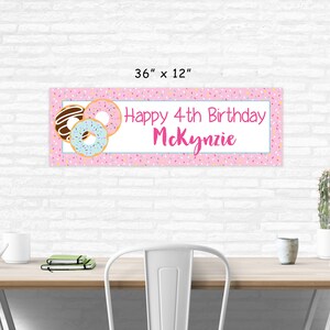Op de afbeelding: Roze en witte donut-thema verjaardagsbord met de tekst "Happy 4th Birthday McKenzie" en kleurrijke sprinkels. De banner is 91,44 cm bij 30,48 cm.