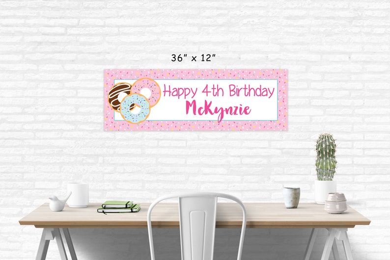 Op de afbeelding: Roze en witte donut-thema verjaardagsbord met de tekst "Happy 4th Birthday McKenzie" en kleurrijke sprinkels. De banner is 91,44 cm bij 30,48 cm.