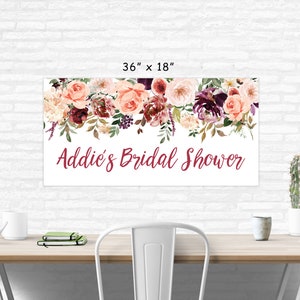 Op de afbeelding: Een witte bruidsdouchebanner met een bloemenkrans van roze, bordeauxrode en witte bloemen. De banner heeft de tekst "Addie's Bridal Shower" in bordeauxrode letters. De banner is 91,44 cm bij 45,72 cm.
