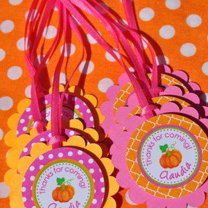 May include: Orange and pink favor tags with a pumpkin design and the text "Thanks for coming! Claudia". The tags are attached to pink ribbon.