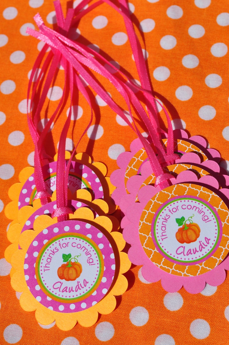 May include: Orange and pink favor tags with a pumpkin design and the text "Thanks for coming! Claudia". The tags are attached to pink ribbon.