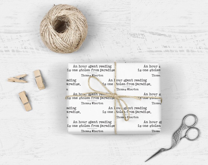 May include: A white gift wrap with a quote from Thomas Wharton: "An hour spent reading is one stolen from paradise." The quote is repeated several times on the wrapping paper.
