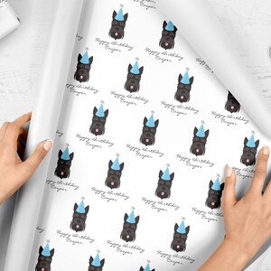 Puede incluir: Papel de regalo blanco con un patr&oacute;n repetido de perros terrier escoceses negros que llevan sombreros de fiesta azules. El texto "Happy Birthday Cooper" se repite en todo el patr&oacute;n.