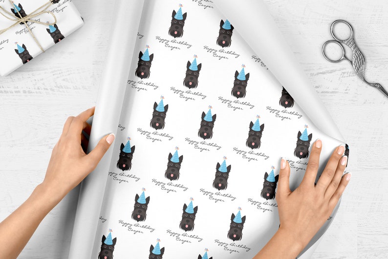 Puede incluir: Papel de regalo blanco con un patr&oacute;n repetido de perros terrier escoceses negros que llevan sombreros de fiesta azules. El texto "Happy Birthday Cooper" se repite en todo el patr&oacute;n.
