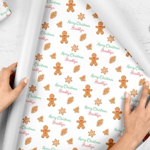 Op de afbeelding: Wit inpakpapier met een herhalend patroon van gingerbread men, sneeuwvlokken, bellen en de tekst "Merry Christmas Brooklyn".