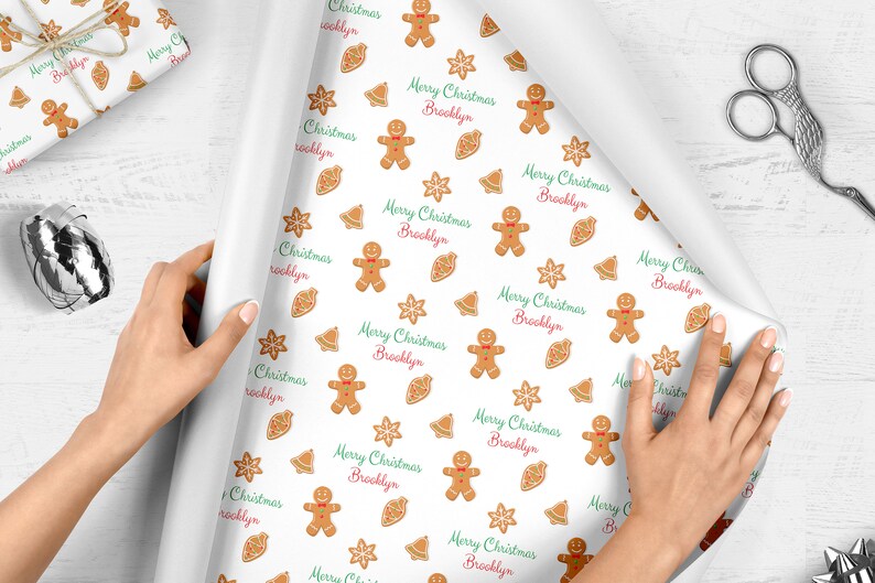 Op de afbeelding: Wit inpakpapier met een herhalend patroon van gingerbread men, sneeuwvlokken, bellen en de tekst "Merry Christmas Brooklyn".