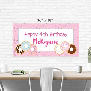 Op de afbeelding: Roze en witte verjaardagsbord met de tekst "Happy 4th Birthday McKenzie" en donut-illustraties. De banner is 91,44 cm bij 45,72 cm.