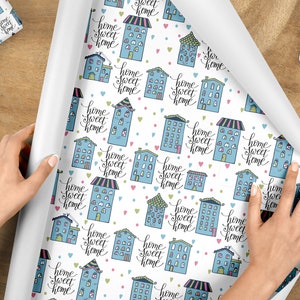 May include: White wrapping paper with a repeating pattern of blue houses with the text "home sweet home" in black script. Pink and green hearts are scattered throughout the pattern.