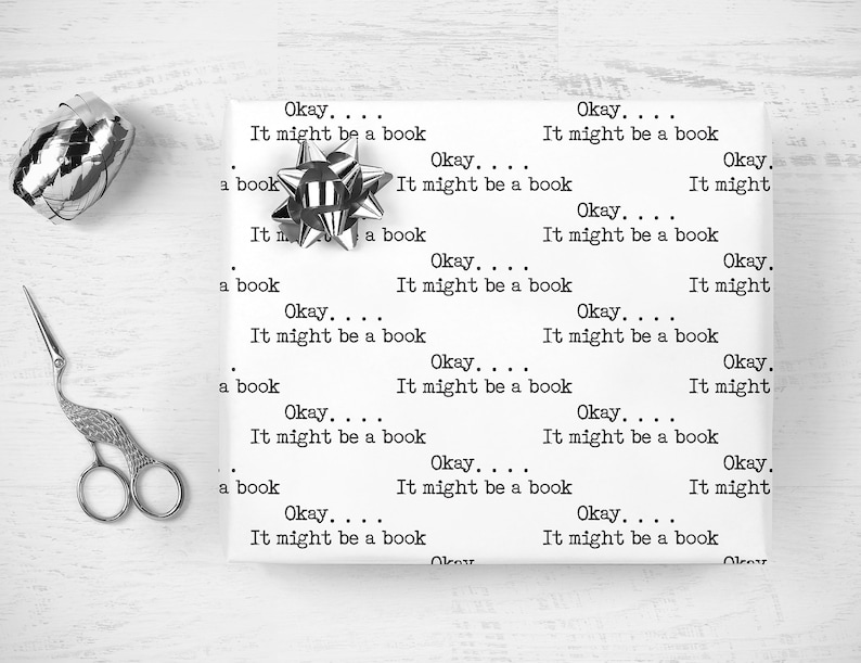 May include: White wrapping paper with the repeated text "Okay... It might be a book" printed on it. A silver bow is on the paper.