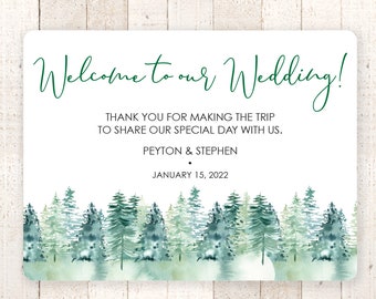 May include: A white wedding welcome sign with green watercolor trees at the bottom. The text reads "Welcome to our Wedding! Thank you for making the trip to share our special day with us. Peyton & Stephen January 15, 2022"