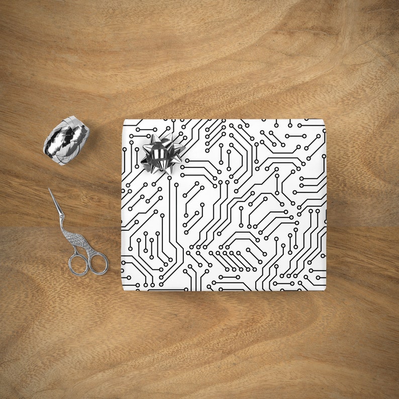 Puede incluir: Papel de regalo blanco con un patr&oacute;n de placa de circuito negro. Un lazo plateado est&aacute; en la parte superior del regalo envuelto.