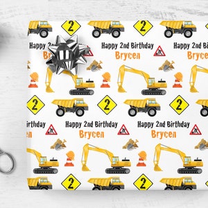 May include: White wrapping paper with a repeating pattern of yellow construction vehicles, including dump trucks, excavators, and construction cones. The text "Happy 2nd Birthday Brycen" is repeated throughout the pattern.