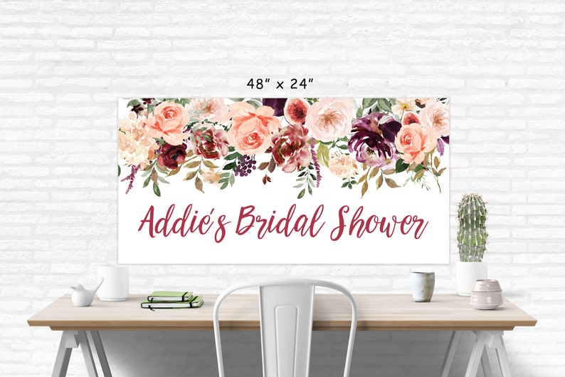 Op de afbeelding: Een witte bruidsdouchebanner met een bloemenkrans van roze, bordeauxrode en witte bloemen. De banner heeft de tekst "Addie's Bridal Shower" in bordeauxrode letters.