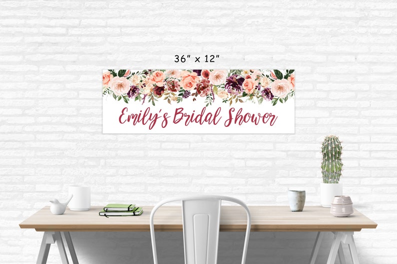 Op de afbeelding: Een witte banner met een bloemenkrans van roze, bordeauxrode en groene bloemen. De banner heeft de tekst "Emily's Bridal Shower" in bordeauxrode schrift. De banner is 91,44 cm breed en 30,48 cm hoog.