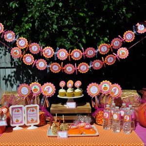 May include: A pink and orange pumpkin-themed first birthday party table setting with cupcakes, a banner that says "Happy 1st Birthday", and a variety of decorations.