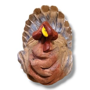 May include: A carved wooden turkey figurine with a detailed, textured surface. The turkey features a brown body, a red wattle and snood, and a yellow beak. The tail feathers are a mix of brown, gray, and white.
