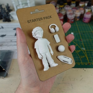Könnte beinhalten: Ein Starter-Set mit weiß bemalten Figuren, darunter eine Person mit Irokesenschnitt, Kopfhörer, ein kleines Rechteck, ein Ball und ein Rettungsring. Das Set ist mit "Starter Pack" beschriftet.