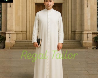Könnte beinhalten: Ein langes, cremefarbenes Priestergewand mit Stehkragen und Knopfleiste. Die Robe wird von einer Person getragen, die ein kleines, schwarzes Buch hält. Das Bild ist vor einem Kirchengebäude aufgenommen. Der Text "Regal Tailor" ist sichtbar.