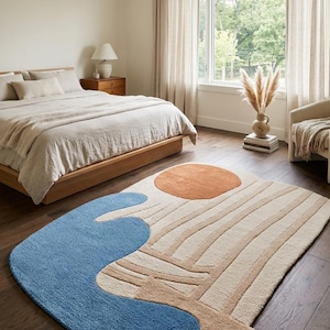 May include: A modern area rug with a unique design. The rug features a blue, tan, and orange color palette. The design includes a blue wave shape, a tan background with vertical lines, and an orange circle. The rug is in a bedroom setting.