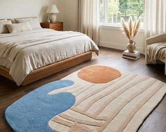 Könnte beinhalten: Moderner Teppich mit einzigartigem Design. Der Teppich hat eine blaue, beige und orange Farbpalette. Das Design umfasst eine blaue Wellenform, einen beigen Hintergrund mit vertikalen Linien und einen orangefarbenen Kreis. Der Teppich befindet sich in einem Schlafzimmer.