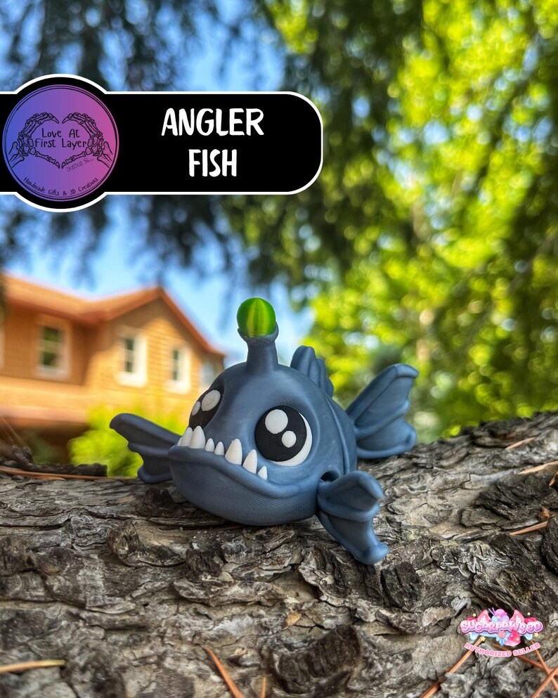 May include: A blue Angler Fish figurine with large white teeth, big black eyes, and a green lure. The figurine is resting on a piece of wood, with the text "Angler Fish" in a black and white banner.