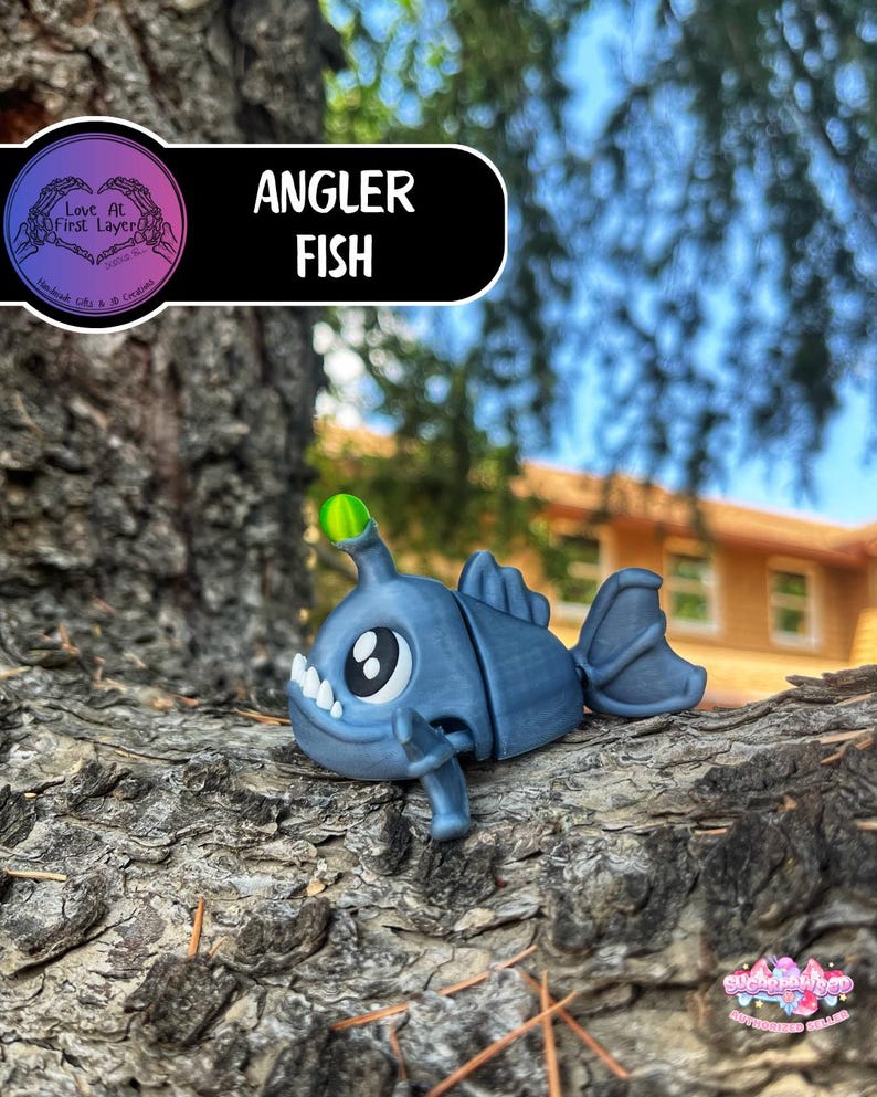 May include: A blue angler fish figurine with a glowing green lure. The figurine has large eyes, sharp teeth, and fins. The text "Angler Fish" is displayed on a black background. The figurine is resting on a tree branch.