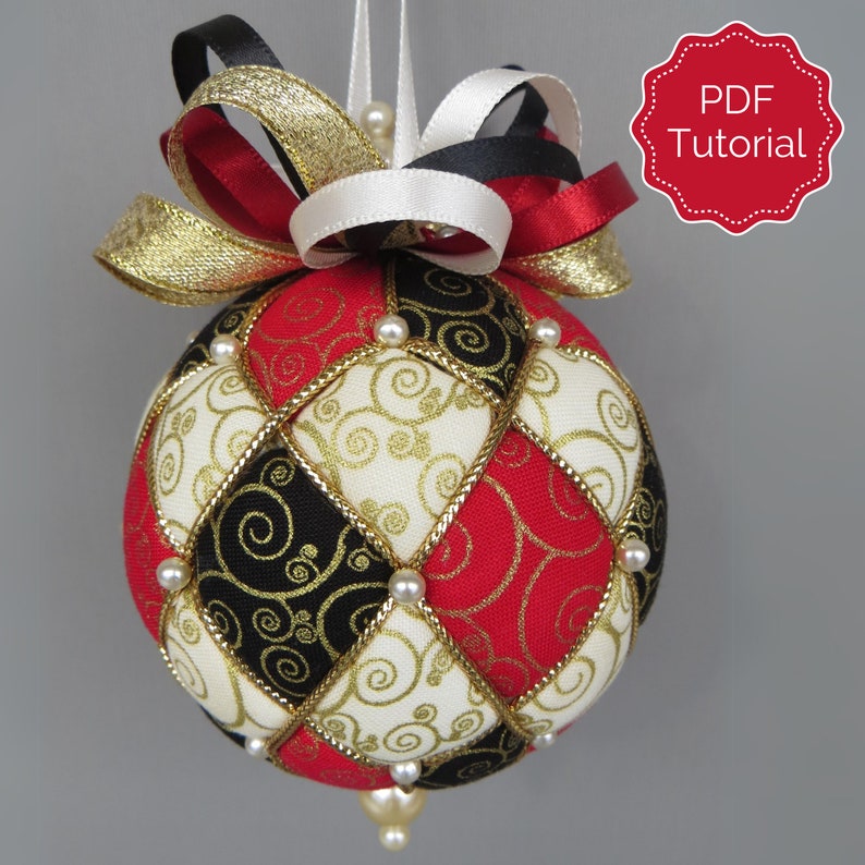 May include: A red, black, and gold fabric Christmas ornament with a white pearl trim and a gold and red ribbon bow. The ornament has a PDF tutorial.