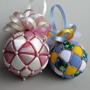May include: Two handmade Christmas ornaments, one pink and white with a pink bow, and one blue, yellow, and green with a blue bow.
