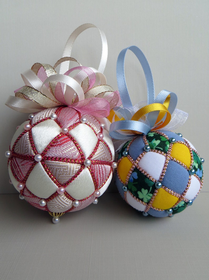 May include: Two handmade Christmas ornaments, one pink and white with a pink bow, and one blue, yellow, and green with a blue bow.