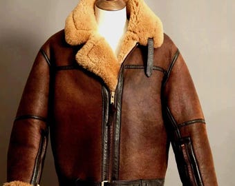 Può includere: Giacca in pelle marrone con colletto e fodera in montone. La giacca presenta una chiusura con zip, una cintura in vita e maniche con zip. La giacca è esposta su un manichino.