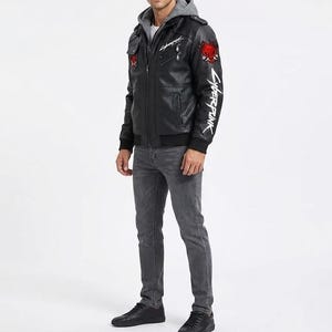 K&ouml;nnte beinhalten: Eine schwarze Kunstlederjacke mit grauem Kapuzeneinsatz, verziert mit einem roten Oni-Masken-Aufn&auml;her auf Brust und Schulter sowie dem in Wei&szlig; gedruckten Schriftzug Cyberpunk auf der Brust und dem linken &Auml;rmel, kombiniert mit grauer Jeans und schwarzen Sneakern.