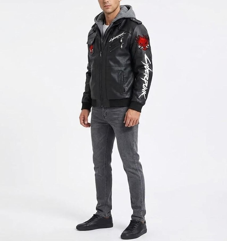 K&ouml;nnte beinhalten: Eine schwarze Kunstlederjacke mit grauem Kapuzeneinsatz, verziert mit einem roten Oni-Masken-Aufn&auml;her auf Brust und Schulter sowie dem in Wei&szlig; gedruckten Schriftzug Cyberpunk auf der Brust und dem linken &Auml;rmel, kombiniert mit grauer Jeans und schwarzen Sneakern.