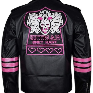 May include: Black leather jacket with pink accents. The back features a pink and white skull emblem with the text "HITMAN BRET HART". Pink stripes adorn the sleeves, and pink hearts are at the bottom of the emblem.